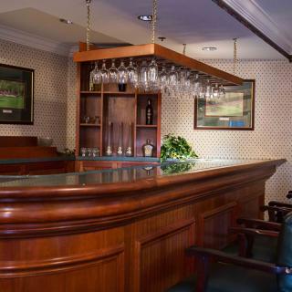 An empty bar with a wooden counter and glasses hanging, creating a cozy atmosphere.