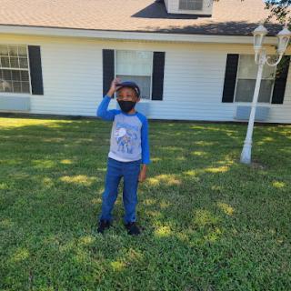 A child standing in the yard, playfully posing with a mask on.