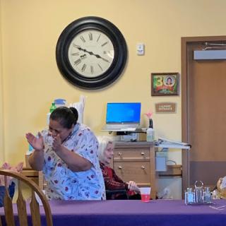 A caregiver engages with an elderly resident in a lively moment at a community center.