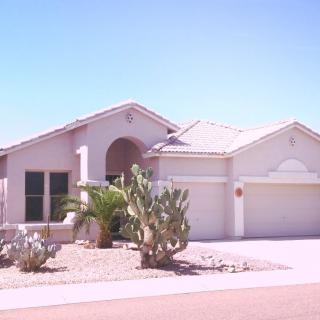 A single-story suburban house with a desert landscape and cactus in the front yard.