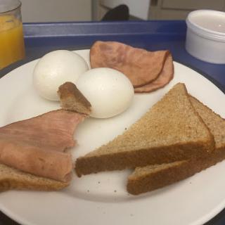 A simple breakfast plate featuring boiled eggs, slices of ham, and toasted bread.