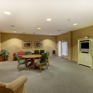 A spacious meeting room featuring a round dining table surrounded by colorful chairs, with a television unit and large windows.
