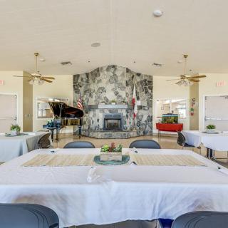 A spacious dining area featuring neatly arranged tables and chairs, with a grand piano and a decorative fireplace as focal points.