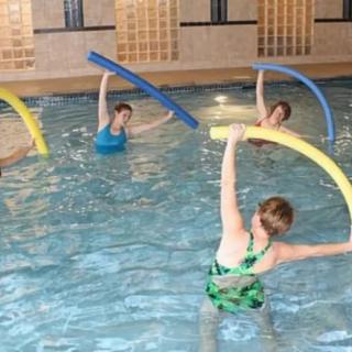 A group of people participating in a water aerobics class using noodles in a swimming pool.