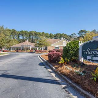 Entrance to a residential community with a sign and landscaped surroundings.