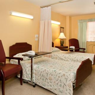 A hospital room with two patient beds, chairs, and privacy curtains.