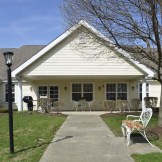 A small house with a porch, featuring chairs and a pathway leading up to it.
