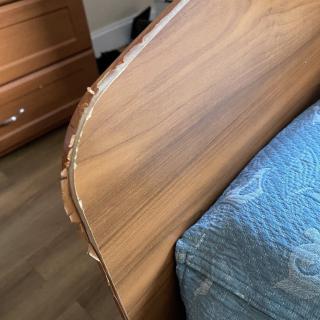 A wooden headboard with visible damage along the edge near a blue-patterned bedspread.