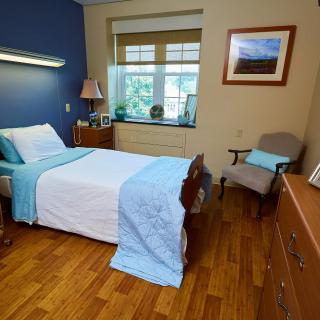 A cozy bedroom with a single bed, wooden floors, and natural lighting from the window.