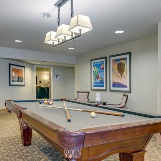 A well-lit game room featuring a billiard table, two chairs, and artwork on the walls.