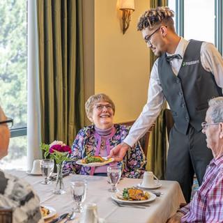 A waiter serves a meal to elderly patrons at a restaurant.