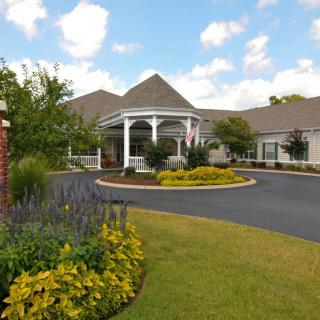 A large building with a landscaped garden and circular driveway under a partly cloudy sky.