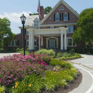 A large house with a well-maintained garden and an American flag on a sunny day.