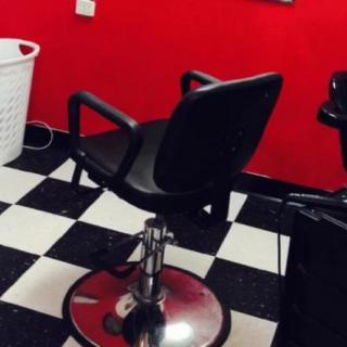 A barber chair in a salon with checkered flooring and red walls.