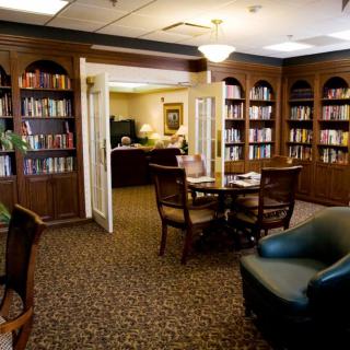 A cozy library room with bookshelves, a table, and chairs arranged for reading.