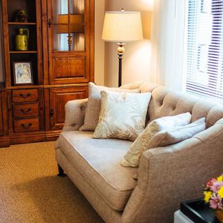 A cozy living room with a beige sofa, decorative pillows, and a wooden cabinet by the window.