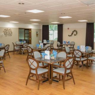 A neatly arranged dining room with multiple tables and chairs, set in a well-lit interior with wooden flooring.