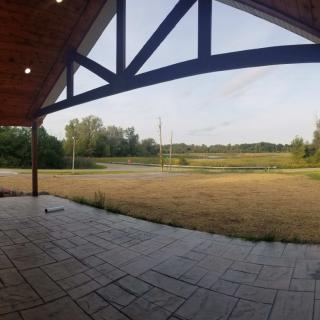 A wide view from a covered patio looking out onto an open field with trees and a clear sky.