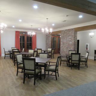 A spacious dining area with tables and chairs, featuring chandeliers and wooden flooring.