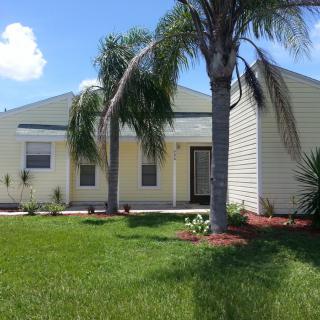 A suburban house with palm trees and a well-maintained lawn under a sunny sky.
