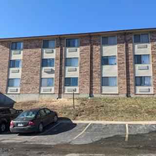 A brick apartment building with a parking lot in front, featuring several parked cars.