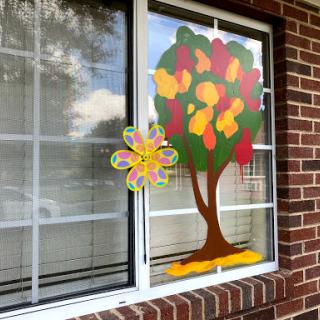 A vibrant and colorful window decoration featuring a fall-themed tree and floral design.