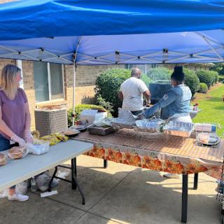 A lively outdoor barbecue gathering with food preparation under a blue tent.