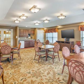 A spacious dining area with multiple tables and chairs, a large television, and a kitchenette in the background.