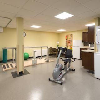 A well-equipped rehabilitation gym featuring an exercise bike, fitness tools, and a kitchenette.