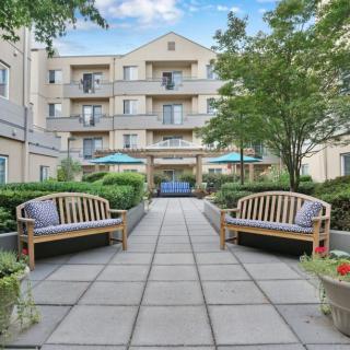 A peaceful courtyard with benches and greenery, surrounded by a multi-story building.