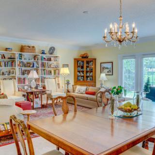 A cozy and well-decorated living space with a dining area, featuring bookshelves, a chandelier, and comfortable seating.