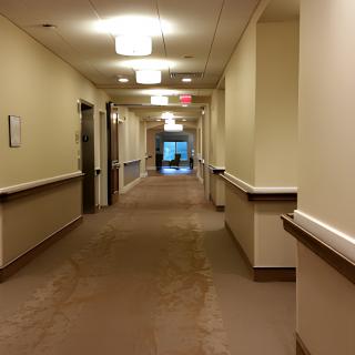A long, well-lit corridor in a building with beige walls and carpeted flooring.