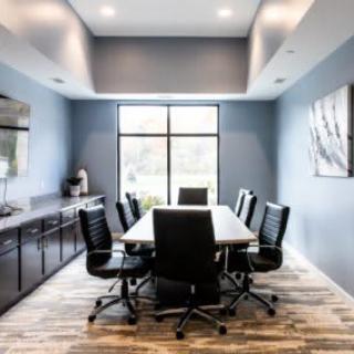 A modern conference room with a large table and leather chairs, illuminated by natural light from a window.