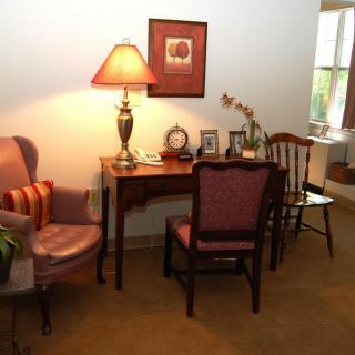 A cozy living room setup featuring a table with framed photos, a lamp, and chairs in a traditional style.