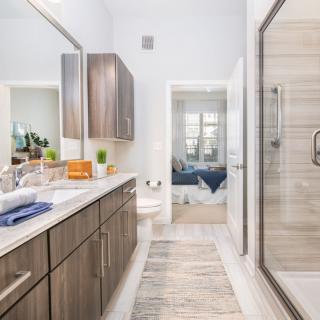 A modern bathroom with wood cabinetry, a large mirror, and a spacious shower.