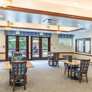 A spacious dining area with tables and chairs, featuring large windows and doors for natural light.