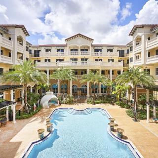 A luxurious resort with a central swimming pool surrounded by palm trees and elegant architecture.