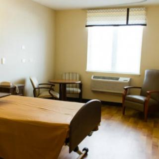 A hospital room with a bed, two chairs, and a window.