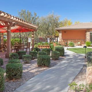 A well-designed outdoor space featuring a patio with tables and chairs, surrounded by lush landscaping under a clear blue sky.