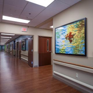 A brightly lit hospital corridor featuring a vibrant painting on the wall.