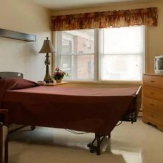 A simple, well-lit bedroom with a single bed, lamp, and dresser.