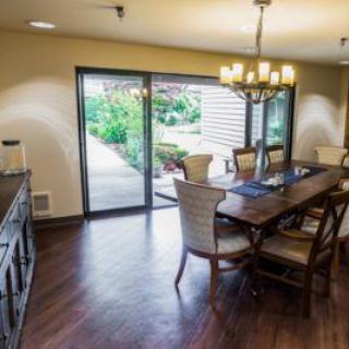 A cozy dining room with a wooden table, chairs, and a chandelier, featuring sliding glass doors that open to a garden view.