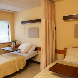 A well-lit hospital patient room featuring two beds separated by a curtain.
