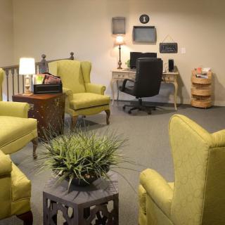 A cozy office space with green chairs, a desk equipped with a computer and a lamp, and decorative elements including a plant.