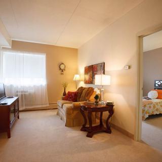 A cozy apartment living room with a sofa, lamps, and a view into the bedroom.