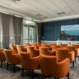 A well-equipped conference room with orange chairs facing a presentation screen.