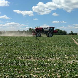 A sprayer applying crop protection products in a lush green field under a clear blue sky.