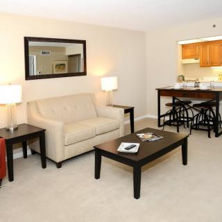 A modern living room with a beige sofa, coffee table, and lamps, facing an open kitchen area.