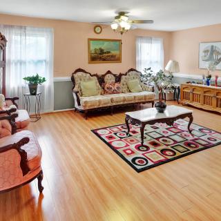 A spacious living room featuring traditional furniture and a patterned rug on hardwood flooring.