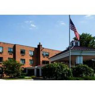 A brick hotel with a flagpole at the entrance, surrounded by trees.